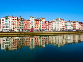 Une rangée de façades bayonnaises aux volets colorés, reflétée dans la Nive