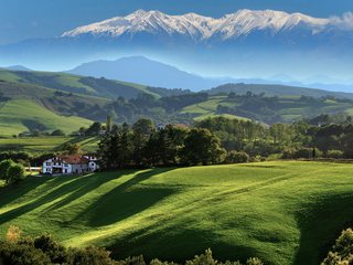 Collines verdoyantes et ferme basque blanche, avec des sommets enneigés à l'horizon
