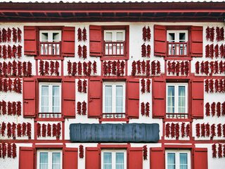 Façade blanche aux volets rouges couverte de guirlandes de piments mis à sécher