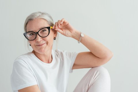 Une femme aux cheveux gris et aux lunettes noires sourit, détendue